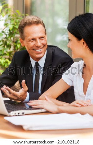 Business meeting. Two business people in formalwear discussing something and smiling while both sitting at the table outdoors