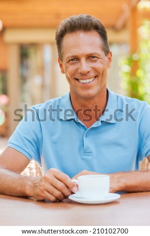 Inspired with cup of fresh coffee. Thoughtful mature man holding hands on chin while sitting in sidewalk cafÃ?Â?Ã?Â© with coffee cup on the table