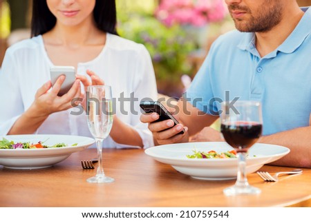 In their separate worlds. Close-up of young couple typing something on their smart phones while relaxing in outdoors restaurant together