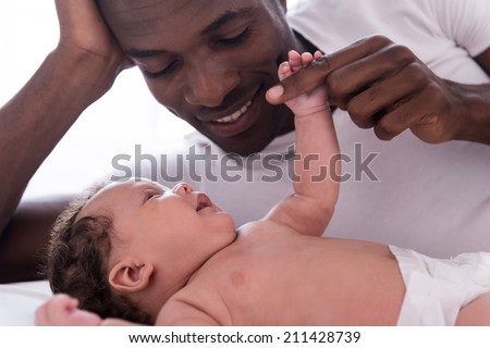 You are my everything! Side view of happy young African man playing with his little baby and smiling while lying in bed