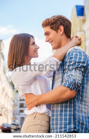 Loving couple. Low angle view of beautiful young loving couple hugging and looking at each other while standing outdoors