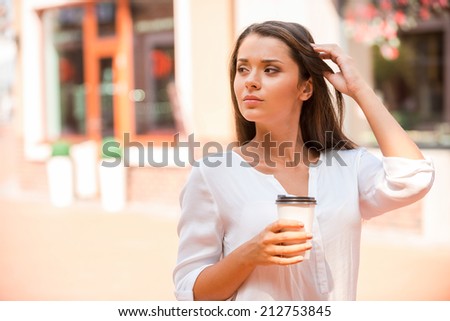 Enjoying fresh coffee on the Go. Beautiful young woman holding coffee cup and looking away while standing outdoors