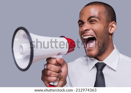 Can you hear me now? Furious young African man in formalwear shouting at megaphone while standing against grey background