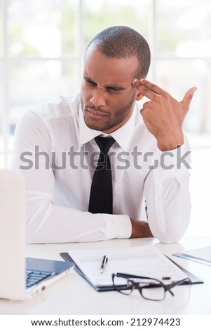 Deadline failed. Frustrated young African man in formalwear touching his temple with finger gun and keeping eyes closed while sitting at his working place