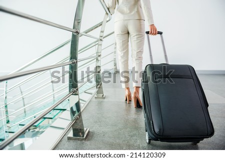 Ready to business trip. Rear view of businesswoman in formalwear carrying suitcase while walking away
