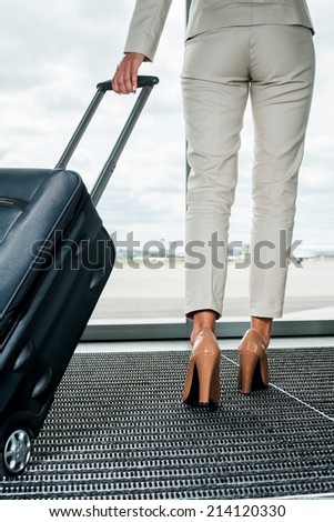 Ready to business trip. Rear view of businesswoman in formalwear carrying suitcase while walking away with airplanes in the background