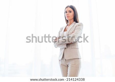 Confident business expert. Confident young businesswoman in suit keeping arms crossed and looking at camera