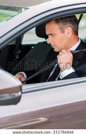 Fastening his seat belt. Confident mature businessman fastening seat belt while sitting in his car