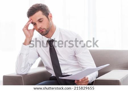 Tired businessman. Depressed young businessman in shirt and tie holding documents while sitting at the chair