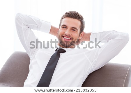 Taking time to relax. Happy young businessman in shirt and tie holding hands behind head and smiling while sitting at the chair