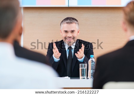 Confident business trainer. Cheerful mature man in formalwear making presentation in conference hall with people on the foreground