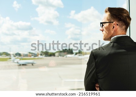 Waiting for his flight. Rear view of thoughtful businessman in formalwear looking through a window in airport