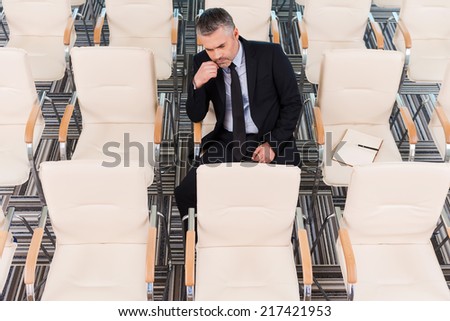 The one and only. Top view of bored mature man in formalwear sitting on the chair in empty conference hall