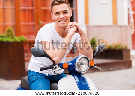 Proud of his new scooter. Handsome young man sitting on scooter and smiling