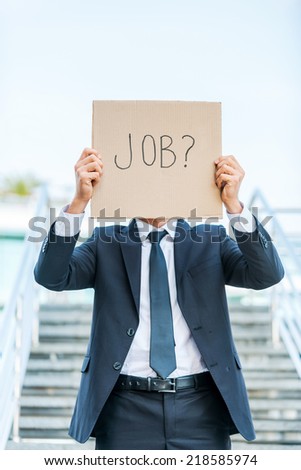 I need a job! Man in formalwear holding poster with job text message in front of his face while standing outdoors and against staircase