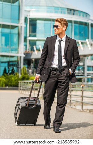Businessman on the Go. Confident young businessman in full suit carrying suitcase while walking outdoors