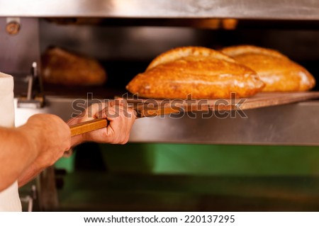 Just baked. Close-up of man taking the fresh baked bread out of oven