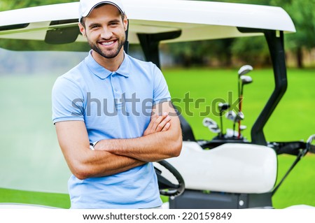 Golf is my favorite game! Handsome young man keeping arms crossed and smiling while leaning at the golf cart while standing on golf course