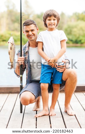 Look what we caught! Father and son looking at camera and smiling while man holding fishing rod with big fish on the hook