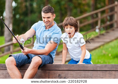 It is a big fish! Happy father and son fishing together while little boy looking excited and keeping mouth open