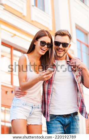 Look at this picture! Low angle view of beautiful young loving couple standing outdoors together and looking at the mobile phone