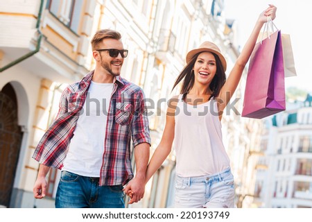 We love shopping together! Beautiful young loving couple walking by the street while beautiful woman carrying shopping bags and smiling