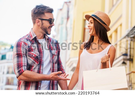 Enjoying their time together. Beautiful young loving couple walking by the street and talking to each other while beautiful woman carrying shopping bags and smiling
