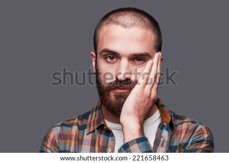 This is too boring. Bored young bearded man keeping arms crossed and expressing ironic smile while standing against grey background