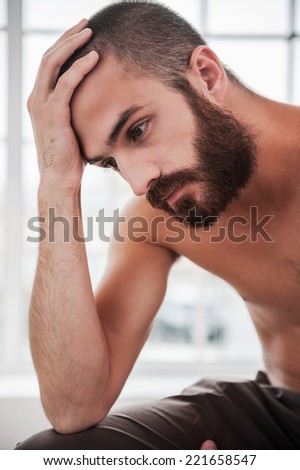 Feeling lonely and depressed. Depressed young bearded and shirtless man holding hand in hair and looking away