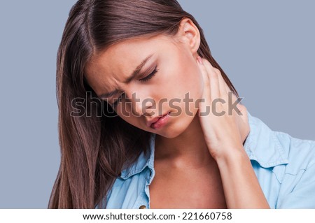 Woman with neck pain. Young woman holding her aching neck standing against grey background