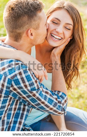Happy together. Young man kissing beautiful cheerful women while she hugging him and looking at the camera.