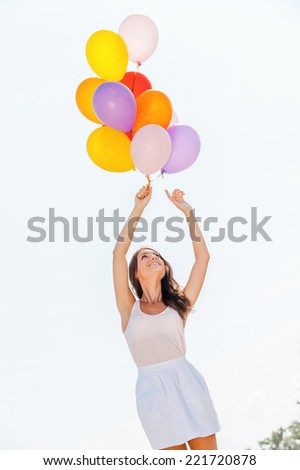 Balloon fun. Low angle view of young beautiful women holding colorful balloons with sky as baclground