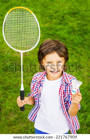 Play badminton? Top view of happy little boy holding badminton racket and shuttlecock while standing on green grass