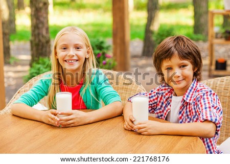 Reloading energy with fresh milk. Two cute little children drinking milk and smiling while sitting outdoors together