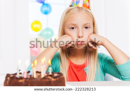 Feeling lonely at her party. Happy little girl looking at the birthday cake and smiling