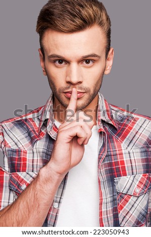 Silence please! Young man giving silence gesture against grey background