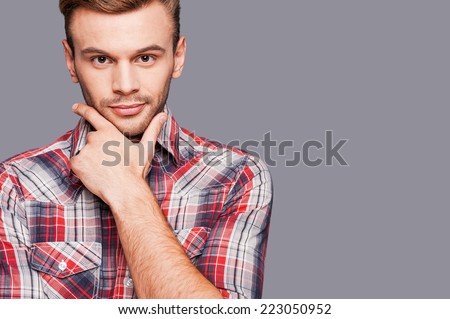Set for success. Confident young man holding hand on chin and looking at camera while standing against grey background