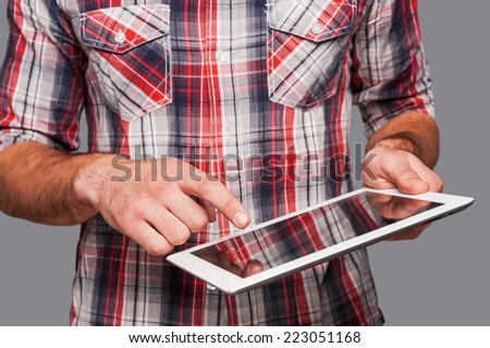 The tablet is so functional! Close-up shot of a man using his tablet while standing against grey background