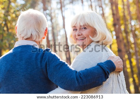 Spending time with husband. Rear view of happy senior woman looking over shoulder and smiling while walking by park with her husband