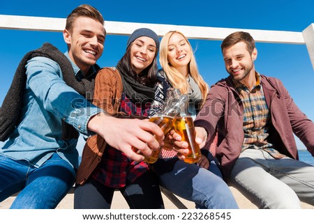 Cheers to friendship! Low angle view of four young cheerful people cheering with beer and smiling while bonding to each other