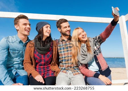 Capturing a happy moment. Low angle view of four happy young people bonding to each other and making selfie while sitting at the riverbank