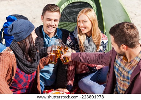 Cheers to us! Top view of four young happy people cheering with beer and smiling while sitting near the tent together