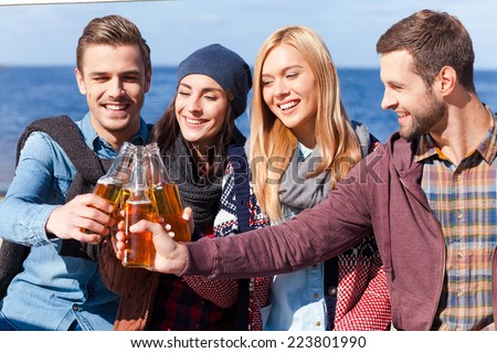 Cheers to friendship! Four young happy people cheering with beer and smiling while bonding to each other