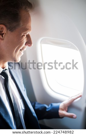 What a great view! Happy mature businessman sitting at his seat in airplane and looking through airplane window