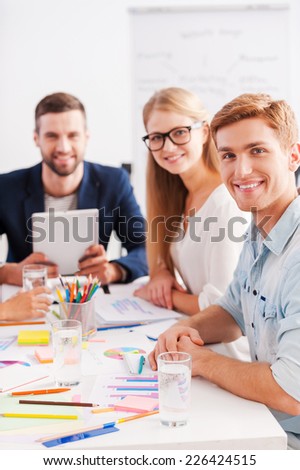 Confident and creative. Group of cheerful business people in smart casual wear sitting together at the table and looking at camera