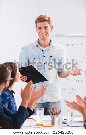 Good job! Group of business people in smart casual wear sitting together at the table and applauding to their colleague standing near whiteboard and smiling