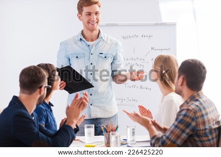 Great presentation! Group of business people in smart casual wear sitting together at the table and applauding to their colleague standing near whiteboard and smiling