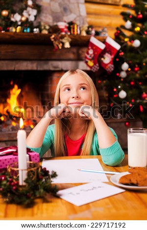 What do I wish? Cute little girl day dreaming while sitting at home with Christmas tree and fireplace in the background