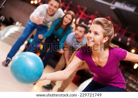 She loves this game. Beautiful young women throwing a bowling ball while three people cheering