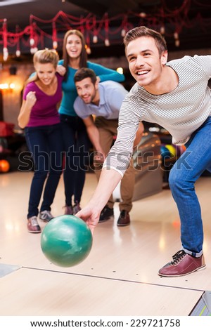He is ready to win. Handsome young men throwing a bowling ball while three people cheering